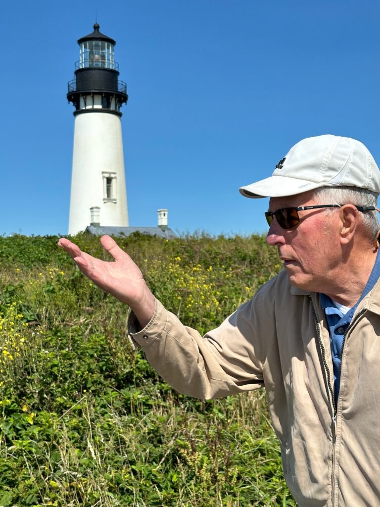 Man standing in an open area in front of a light house