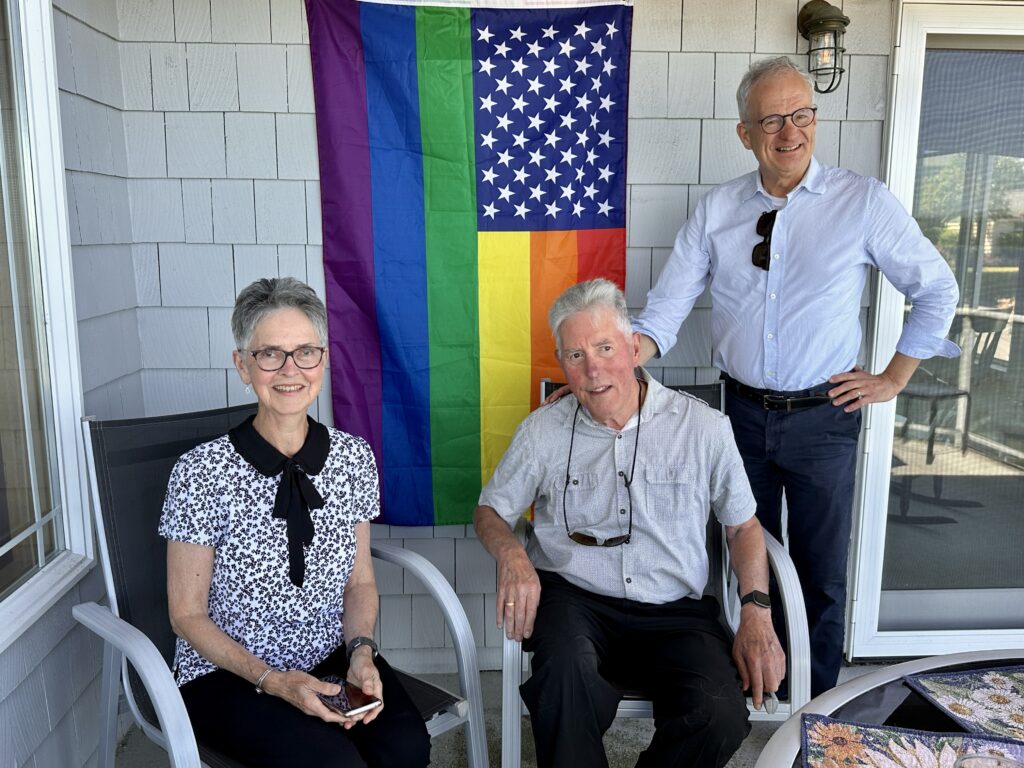 three people on a deck in front of a pride flag
